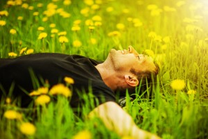 Happy smiling man lying on grass with yellow dandelion at sunny day